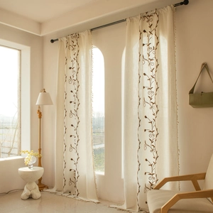 Detailed close-up of cream linen curtains with brown floral embroidery and ball fringe trim