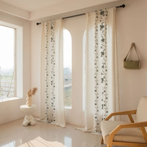 Detail view of vintage beige cotton linen curtain with green floral embroidery and tassels
