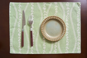Sottopiatto verde con motivi floreali bianchi su tavolo in legno con posate