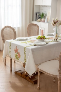 Détail de broderie florale rose et franges à glands sur nappe en lin beige