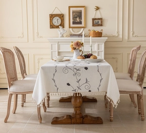 Close-up of grey floral embroidery and decorative tassels on beige cotton tablecloth