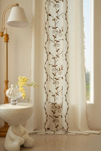 Detail of beige linen curtain featuring elegant vine embroidery and delicate side tassels