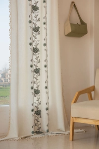 Detail of beige cotton linen curtain featuring green floral embroidery and elegant tassels