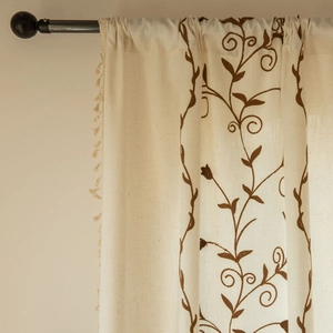 Detail of beige cotton linen curtain with floral embroidery and tassel fringe decor
