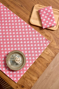 Detail of pink cotton-linen napkin with white heart patterns on rustic wooden table