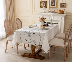 Detail of floral printed linen tablecloth with tassel edges on a wooden table