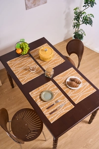 Set di quattro tovagliette gialle con motivi floreali su un tavolo di legno scuro