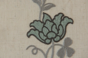 Close-up of elegant floral embroidery on beige linen curtain with intricate gray stitching