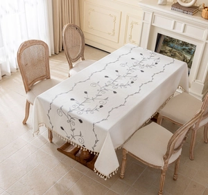 Detailed embroidery of gray floral vines and fringe tassels on a cream linen tablecloth