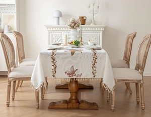 Détail de broderie florale et franges sur une nappe rectangulaire de couleur crème