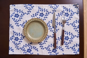 Detail of floral linen placemat with blue blossoms under a ceramic plate and cutlery
