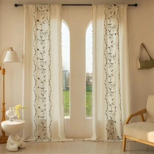 Detail of beige cotton linen curtain with black vine embroidery and fringe tassels