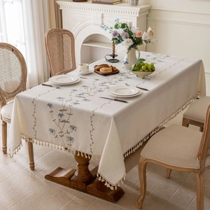French cream floral embroidered tablecloth with tassels on a rustic dining table
