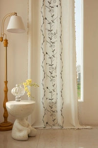 Detailed embroidery of vines and fringe tassels on beige linen-textured window curtains