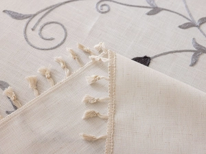 Detail of floral vine embroidery and tassel fringe on beige cotton linen tablecloth