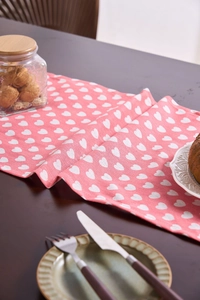 Detail of pink table runner with heart patterns on a dark wood dining table setup
