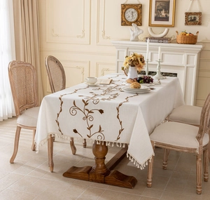Close-up of beige rectangular tablecloth with brown vine embroidery and fringe tassels