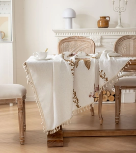 Gros plan sur la broderie florale vintage et les franges beiges de la nappe en lin