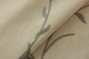 Close-up of beige linen curtain with intricate green leaf vine embroidery and tassels