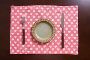 Close-up of pink floral placemat with white heart patterns on a wooden table