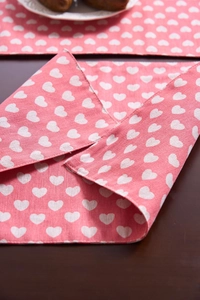 Detalle de mantel individual de tela rosa con estampado de corazones blancos