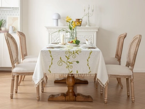 Close-up of rural style beige tablecloth with green vine embroidery and tassel edges