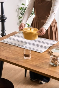Detail of yellow round cast iron enamel pot on a striped fabric napkin on wooden table
