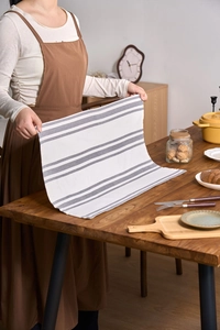 Detail view of gray and white striped cotton linen napkin held by hands over wooden table