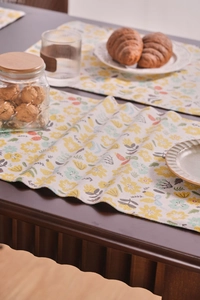 Detalle de mantel individual de tela con flores francesas en mesa de madera oscura cálida