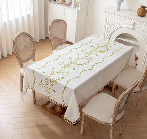 Close-up of green vine embroidery and handmade tassels on beige linen tablecloth