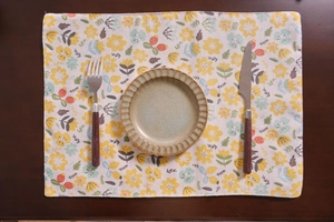 Detalle de mantel individual de tela con flores amarillas sobre mesa de madera y plato