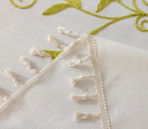Detail of embroidered green leaf vine on cream linen tablecloth with cotton tassel edge