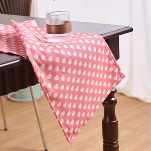 Pink table runner with white heart pattern draped over a dark wooden table edge