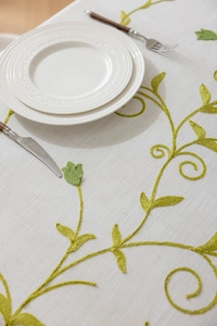 Detailed close-up of green vine floral embroidery on a beige cotton linen tablecloth