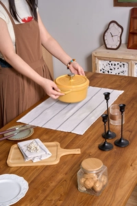 Close-up of hands holding a yellow cast iron pot on a striped fabric placemat