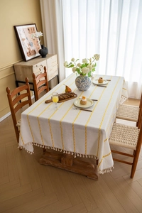 Close-up of beige linen tablecloth with yellow embroidery and tassel fringe details