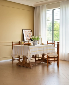 Detail view of cream tablecloth with yellow vertical embroidery and fringe edges