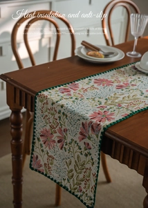 Detail of floral jacquard table runner with pink lily patterns and wavy green stitched edges