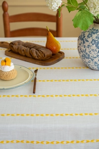 Close-up of yellow heart embroidery on cream tablecloth with natural cotton linen texture