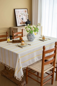 Detail of cream linen tablecloth with yellow embroidery lines and beige tassels on wood