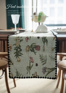 Detail of floral table runner with pom pom trim and thermal insulation on wood table