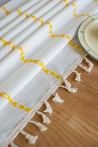 Detail of white cotton linen tablecloth featuring yellow embroidery and beige tassels
