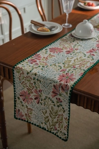 Detail of floral table runner with pink lily embroidery and dark green lace edging
