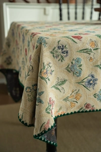Detail of floral jacquard tablecloth with scalloped green edges and woven texture