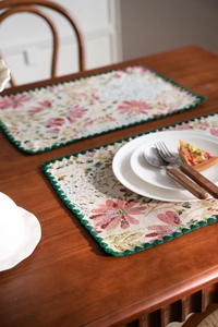 Detail of floral jacquard place mat with green scalloped lace trim on a wood table