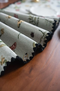 Detail of floral butterfly pattern on green table runner with black scalloped lace edge