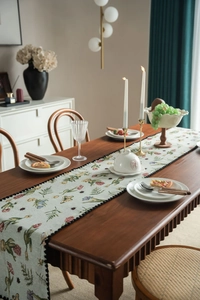 Close-up of pastoral floral table runner with blue green base and black pompom lace edge