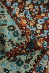 Detail of French vintage floral jacquard tablecloth with tassel trim and leopard pattern
