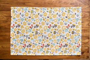 Detail of floral cotton linen napkin with yellow prints on a rustic wooden table surface