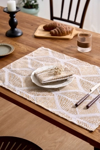 Detail of fabric placemat and napkin with golden geometric patterns on dark wood